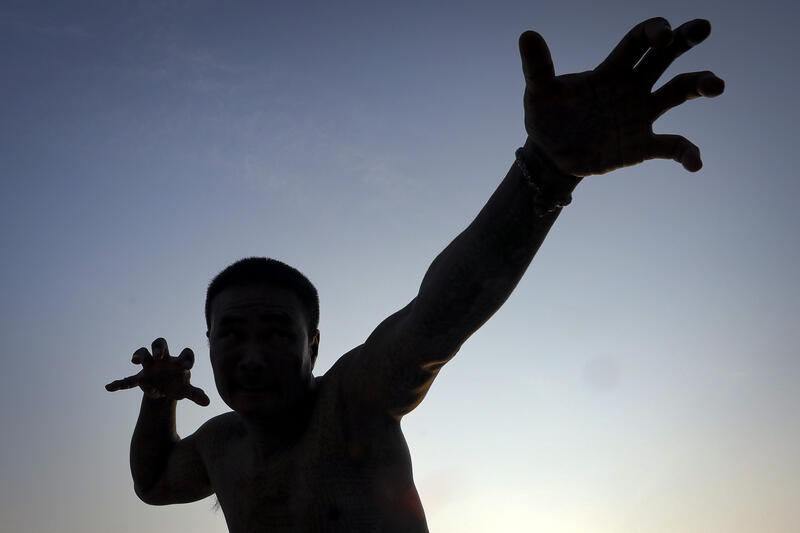 A devotee in a trance, believed to be possessed by the spirits of the animal tattooed on his skin, during the annual Magic Tattoo Festival at Wat Bang Phra in Nakhon Pathom province, Thailand, 23 March 2024. The Magic Tattoo Festival, also known as the 'Wai Khru Ceremony' (Wai Khru means 'honour the teacher'), attracts devotees from across the country who travel to Wat Bang Phra monastery to receive their traditional tattoos and pay their respects to the temple's master tattooist during the Magic Tattoo Festival. During the festival, devotees sit facing the main shrine before many, 'possessed' by the spirit of the animal tattooed on their skin, stand up, mimic the animal's behaviour and eventually make their way towards the main shrine, sometimes running at high speed, until they are stopped by a group of helpers and medics who bring them out of the trance by rubbing their ears. Receiving a Sak Yant is highly respected in Thailand, and many believe the tattoos have mystical powers to ward off bad luck and protect people from harm. Matrix Images / Diego Azubel